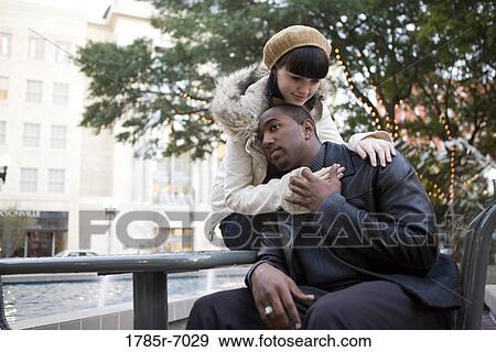 Stock Photo - Young inter-racial couple embracing on a park bench. Fotosearch