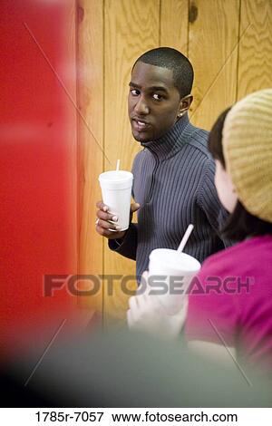 Stock Photo - Young inter-racial couple holding drink cups in a diner. Fotosearch