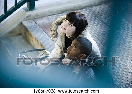 Young inter-racial couple sitting at the top of a flight of stairs at a public train station View Large Photo Image Stock Photo - Young inter-racial couple sitting at the top of a flight of stairs at a public train station. Fotosearch