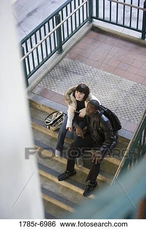 Stock Photograph - Young inter-racial couple sitting at the bottom of a flight of stairs at a public train station. Fotosearch