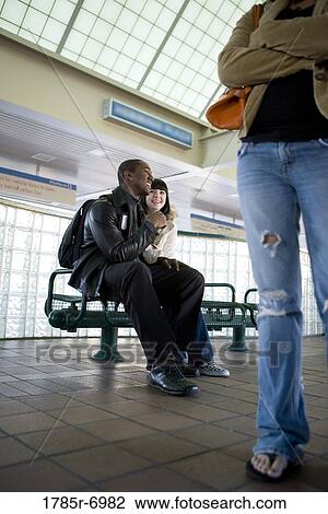 Young inter-racial couple sitting on a bench at a public train station View Large Photo Image Stock Image - Young inter-racial couple sitting on a bench at a public train station. Fotosearch