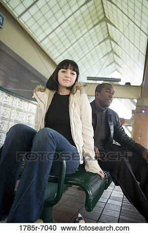 Young inter-racial couple sitting on a bench at a public train station View Large Photo Image Stock Image - Young inter-racial couple sitting on a bench at a public train station. Fotosearch