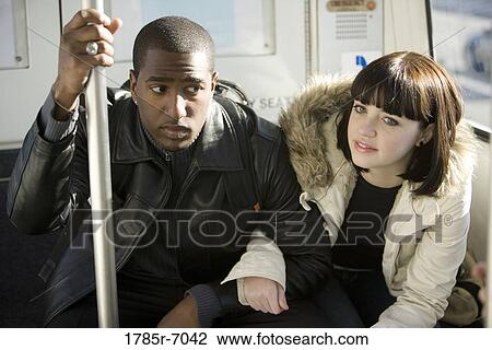 Stock Image - Young inter-racial couple traveling in a mass transit train. Fotosearch