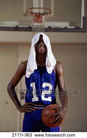 Stock Image - Young man standing holding a basketball with a towel on his head. Fotosearch