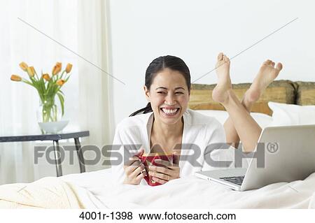 Young woman drinking coffee on the bed and smiling View Large Photo Image Stock Photo - Young woman drinking coffee on the bed and smiling. Fotosearch