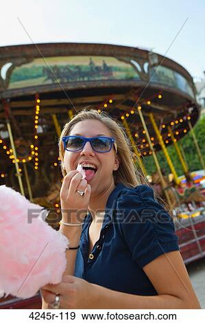 Stock Photo - Young woman eating cotton candy in front of a carousel, Place De La Concorde, Paris, Ile-de-France, France. Fotosearch