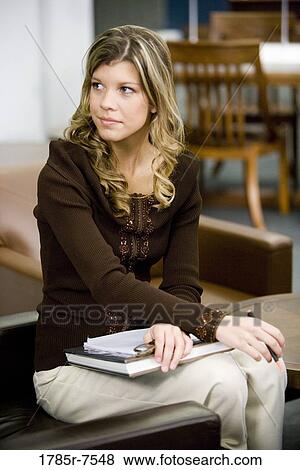 Stock Photo - Young woman holding a book sitting in a library. Fotosearch