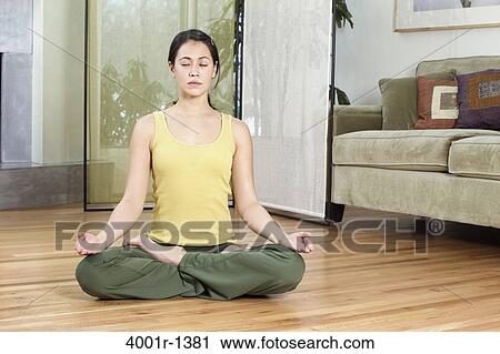 Stock Image - Young woman meditating at home. Fotosearch