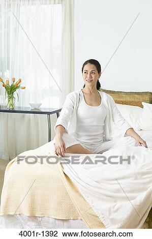 Young woman sitting on the bed in her bedroom View Large Photo Image Stock Image - Young woman sitting on the bed in her bedroom. Fotosearch