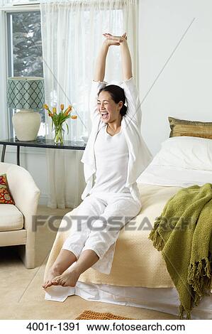 Stock Image - Young woman stretching on the bed and laughing. Fotosearch