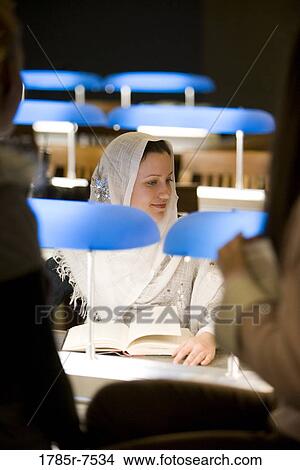 Young woman wearing a head scarf sitting in the reading room of a library View Large Photo Image Picture - Young woman wearing a head scarf sitting in the reading room of a library. Fotosearch