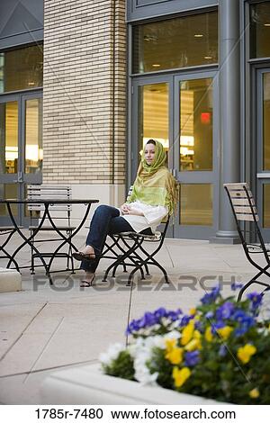 Young woman wearing a head scarf sitting at a table outside a building View Large Photo Image Stock Image - Young woman wearing a head scarf sitting at a table outside a building. Fotosearch