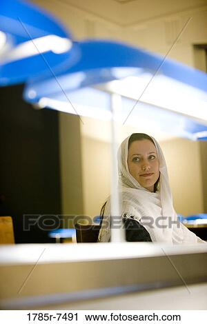 Young woman wearing a head scarf sitting in the reading room of a library View Large Photo Image Stock Image - Young woman wearing a head scarf sitting in the reading room of a library. Fotosearch