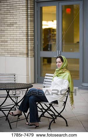Young woman wearing a head scarf sitting at a table outside a building View Large Photo Image Stock Photo - Young woman wearing a head scarf sitting at a table outside a building. Fotosearch