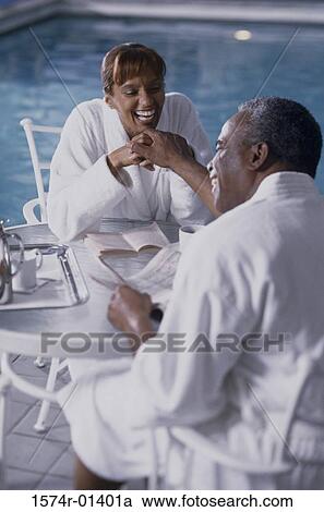 Stock Image - Couple sitting beside a swimming pool. Fotosearch