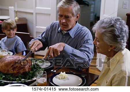Stock Photography - Grandparents carving a turkey at the dining table with their grandson. Fotosearch