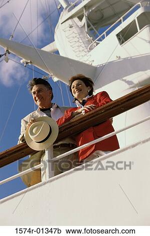Stock Image - Low angle view of a couple standing against the railing of a ship. Fotosearch
