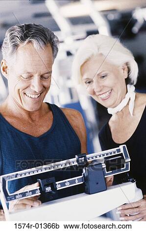 Stock Image - Man standing on a weighing scale. Fotosearch