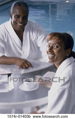Stock Image - Portrait of a couple sitting beside a swimming pool. Fotosearch