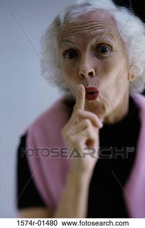 Stock Image - Portrait of a senior woman holding her finger up to her lips. Fotosearch