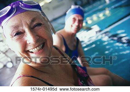 Stock Image - Portrait of two senior women sitting at the edge of a swimming pool. Fotosearch