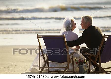 Rear view of a bride and bridegroom sitting on the beach View Large Photo Image Stock Image - Rear view of a bride and bridegroom sitting on the beach. Fotosearch