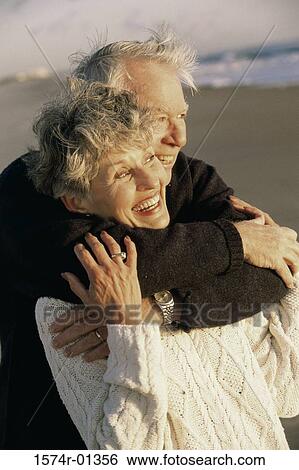 Stock Photograph - Senior couple holding each other at the beach. Fotosearch