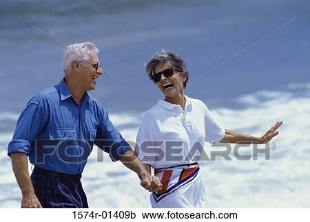 Stock Image - Senior couple holding hands at the beach. Fotosearch