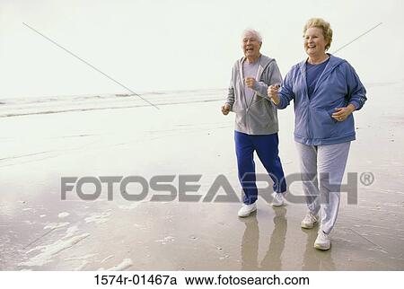 Stock Image - Senior couple jogging at the beach. Fotosearch