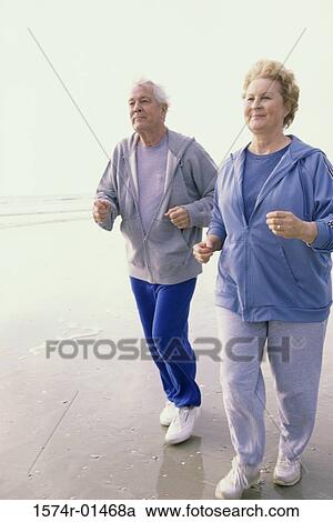 Stock Image - Senior couple jogging at the beach. Fotosearch