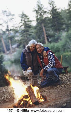 Stock Image - Senior couple together near a campfire in the woods. Fotosearch