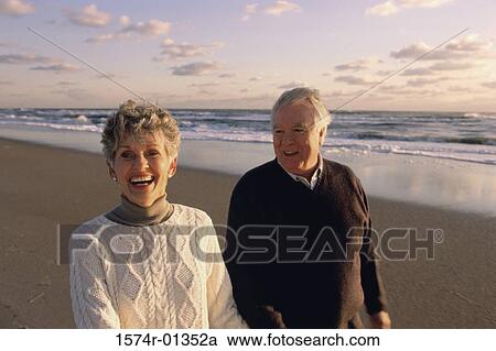 Stock Image - Senior couple walking on the beach. Fotosearch