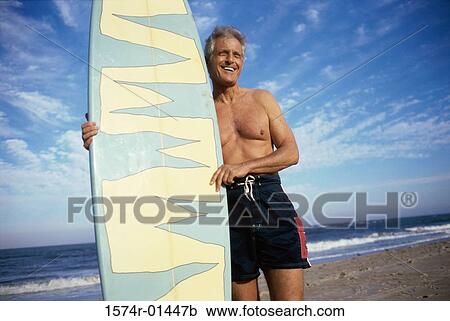 Senior man at the beach holding a surfboard View Large Photo Image Stock Image - Senior man at the beach holding a surfboard. Fotosearch