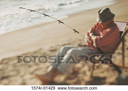Senior man sitting on a beach chair with a fishing rod View Large Photo Image Stock Photo - Senior man sitting on a beach chair with a fishing rod. Fotosearch