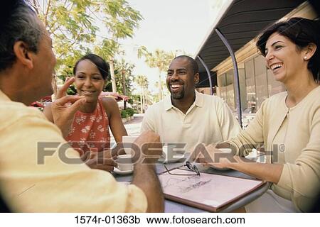 Stock Image - Two couples sitting at a table outdoors. Fotosearch