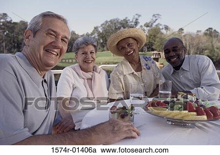 Stock Image - Two elderly couples sitting at a table outdoors. Fotosearch