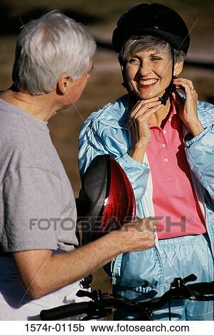 Stock Image - Woman putting on a cycling helmet standing with a man. Fotosearch
