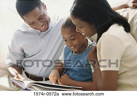 Father and mother sitting on a sofa with their daughter reading a book View Large Photo Image Stock Image - Father and mother sitting on a sofa with their daughter reading a book. Fotosearch