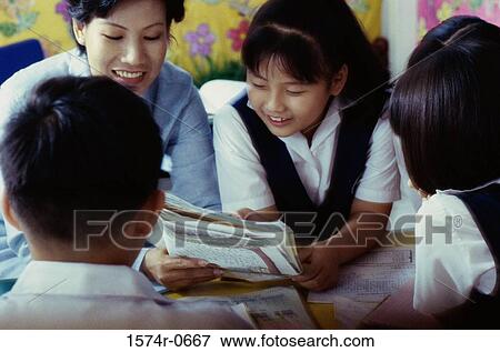 Stock Photo - Female teacher holding a book with her students in class. Fotosearch