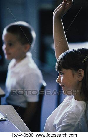 Stock Image - Girl raising her hand in a classroom. Fotosearch