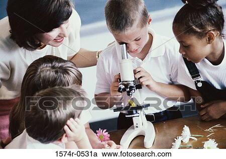 Stock Image - High angle view of school children peering through a microscope with a teacher nearby. Fotosearch