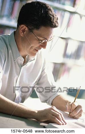 Man sitting at a desk writing in a notebook with a pencil View Large Photo Image Stock Photo - Man sitting at a desk writing in a notebook with a pencil. Fotosearch