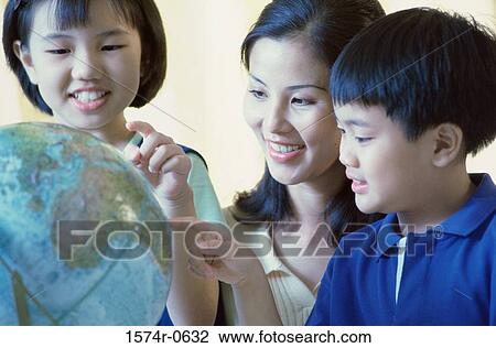 Stock Image - Mother and her two children pointing to a globe. Fotosearch