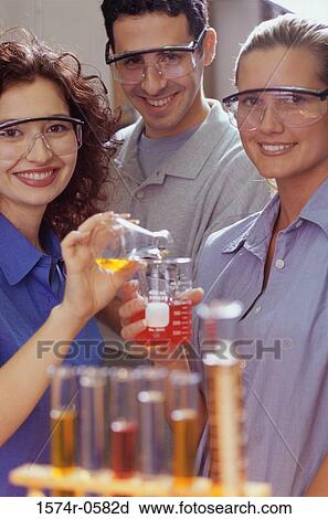Stock Image - Portrait of two young women and a young man performing an experiment in a chemistry laboratory. Fotosearch