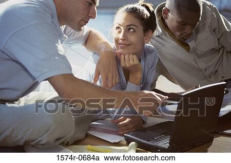 Stock Image - Two young men and a young woman studying together. Fotosearch