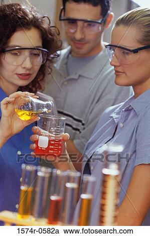 Stock Image - Two young women and a young man performing an experiment in a chemistry laboratory. Fotosearch