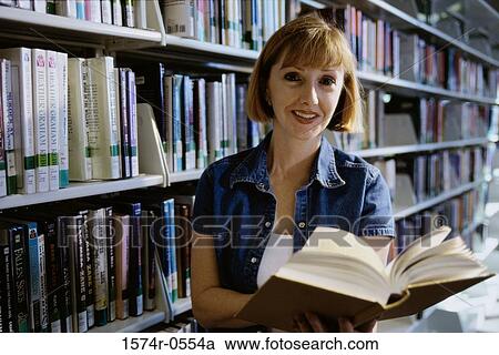 Young woman holding a book in a library View Large Photo Image Stock Image - Young woman holding a book in a library. Fotosearch
