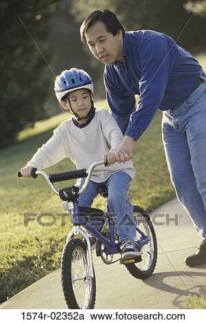 Father helping his son ride a bicycle View Large Photo Image Stock Image - Father helping his son ride a bicycle. Fotosearch