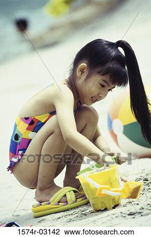 Stock Image - Girl playing in the sand on the beach. Fotosearch