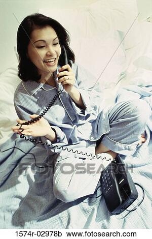 High angle view of a young woman sitting on a bed talking on a telephone View Large Photo Image Stock Image - High angle view of a young woman sitting on a bed talking on a telephone. Fotosearch